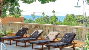 Tres sillones de madera con cojines, un barandal de piedra y vista al mar.