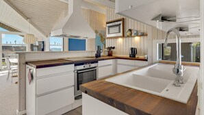 Une cuisine moderne avec des meubles blancs, un plan de travail en bois, un four encastré, un évier et une vue sur l’extérieur.