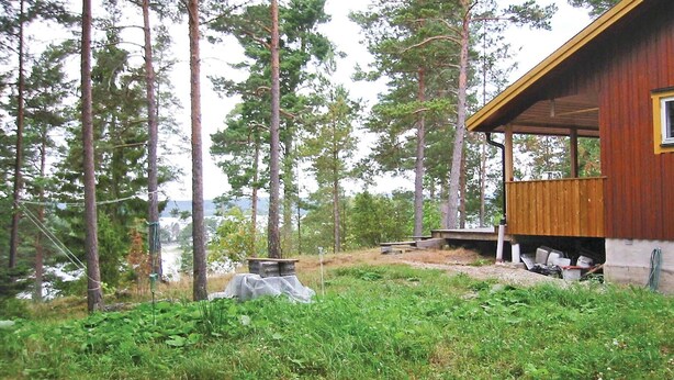 Eine Holzhütte mit Veranda und Blick auf ein bewaldetes Gebiet mit hohen Bäumen.