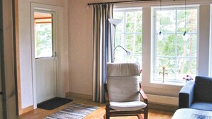 Ein Zimmer mit Holzbalkendecke, einem Sessel, einer Couch und großen Fenstern mit Vorhängen.