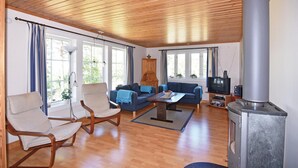 Ein gemütliches Wohnzimmer mit Holzboden, einer Sofagarnitur, einem Sessel, einem Fernseher und einem Kaminofen.