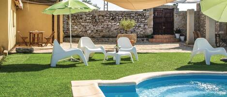 A backyard with a swimming pool, white plastic chairs, and umbrellas.