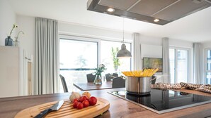 A modern kitchen with a wooden countertop, a cutting board with tomatoes, a pot of spaghetti, and a dining area in the background. - Apartment Haffperle - Oasis on the lagoon - Haffperle (1-4) (Garz/Usedom)