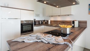 A modern kitchen with stainless steel appliances, a wooden countertop, and a stainless steel pot of spaghetti. - Apartment Haffperle - Oasis on the lagoon - Haffperle (1-4) (Garz/Usedom)