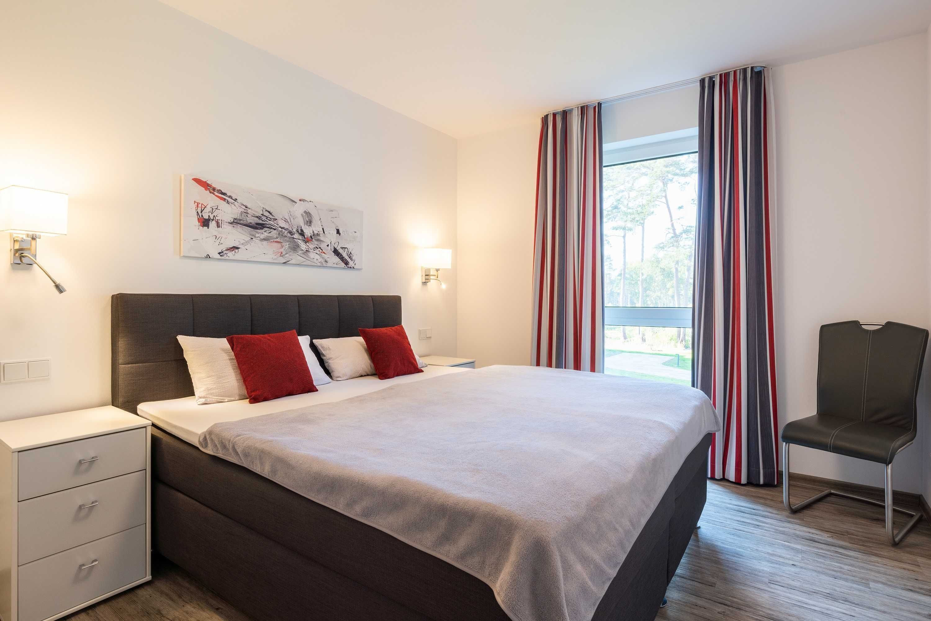 Ein modernes Hotelzimmer mit einem großen Bett, Nachttischen, einem Sessel und einem Fenster mit Vorhängen.