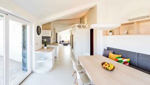 Une cuisine moderne avec un coin repas, comprenant une table en bois, des chaises blanches et un canapé agrémenté de coussins colorés.