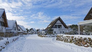 En snötäckt gata med traditionella hus, en stenmur och en klar himmel.
