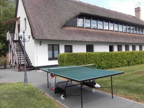 En bygning med stråtækt tag, en trappe og et grønt bordtennisbord i forgrunden.