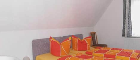Ein Schlafzimmer mit einem Bett, einem Nachttisch, einer Lampe und einem Fenster mit Vorhängen.