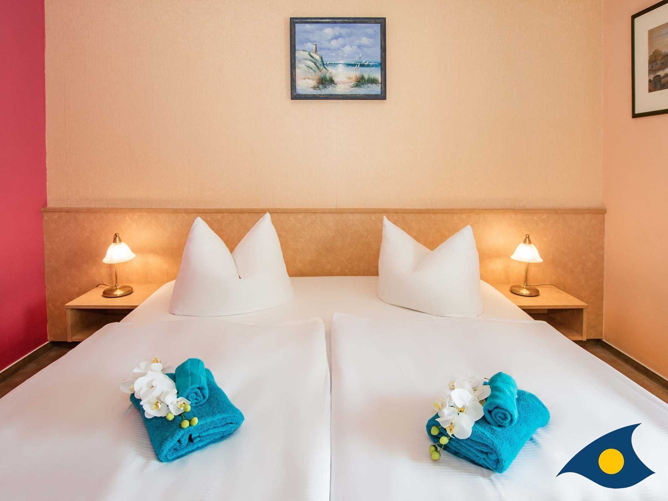 Ein Hotelzimmer mit zwei Betten, weißen Leinentextilien, passenden Kissen, Nachttischlampen und einem Bild an der Wand.