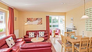 A living room with a red sofa, a round coffee table, and a dining area with a wooden table and chairs. - Villa Cosima - VC 13 (Heringsdorf)