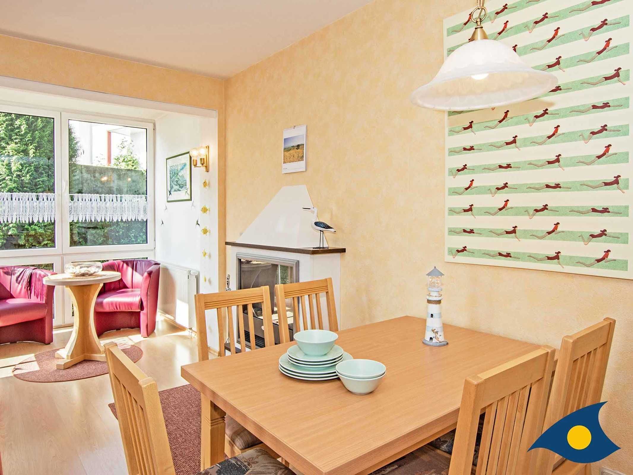 Ein gemütlicher Essbereich mit einem Holztisch, gedeckt für vier Personen, umgeben von Holzstühlen. Es gibt einen kleinen runden Tisch mit einer Glasbowl und einer weißen Lampe an der Wand.