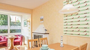 A cozy dining area with a wooden table set for four, surrounded by wooden chairs. There is a small round table with a glass bowl and a white lamp on the wall. - Villa Cosima - VC 13 (Heringsdorf)