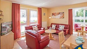 A cozy living room with red leather sofas, a wooden coffee table, and a TV on a wooden cabinet. - Villa Cosima - VC 13 (Heringsdorf)