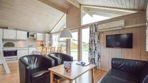 Eine moderne Küche mit weißen Schränken, einer Mikrowelle und einem Herd. Es gibt einen Essbereich mit Tisch und Stühlen sowie ein Wohnzimmer mit einer Couch und einem Fernseher.
