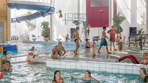 Ein Hallenbad mit mehreren Bahnen, einem Sprungbrett und einer Wasserrutsche.