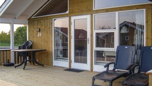 Ein überdachter Außenbereich mit Holzterrasse, Tisch und Stühlen sowie großen Schiebeglastüren, die zu einem Haus führen.