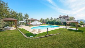 Un jardin avec une piscine, des chaises longues et deux pergolas.