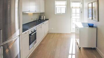 A modern kitchen with stainless steel appliances, a black countertop, and a wooden floor.
