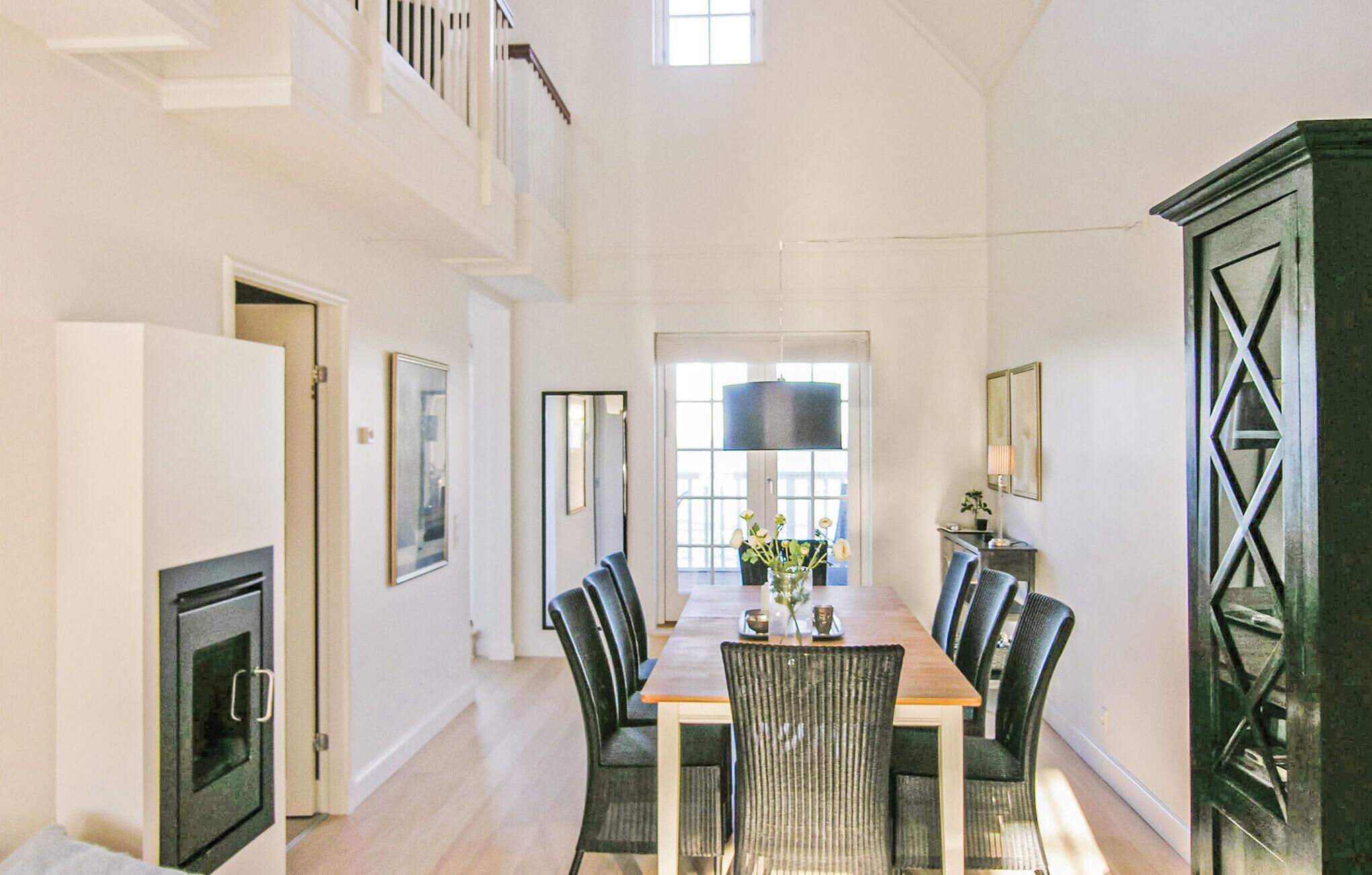 A spacious dining area with a long wooden table and multiple chairs, a large window with natural light, and a staircase leading to an upper level.