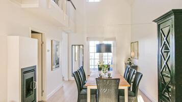 A spacious dining area with a long wooden table and multiple chairs, a large window with natural light, and a staircase leading to an upper level.