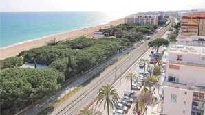 A coastal hotel with a view of the beach, a parking area, and a road with vehicles.