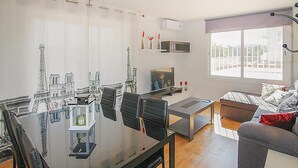 A modern living room with a glass dining table, black chairs, a grey sofa, and a television.