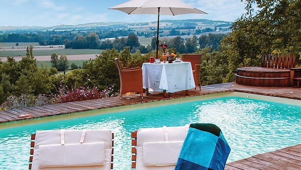 A pool area with two lounge chairs, a table with a white tablecloth, and an umbrella. - Awesome home in Masseube with sauna (Masseube)