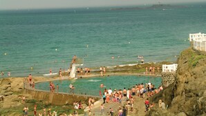 Ein Küsten-Badebereich mit mehreren Pools und einem Leuchtturm im Hintergrund.