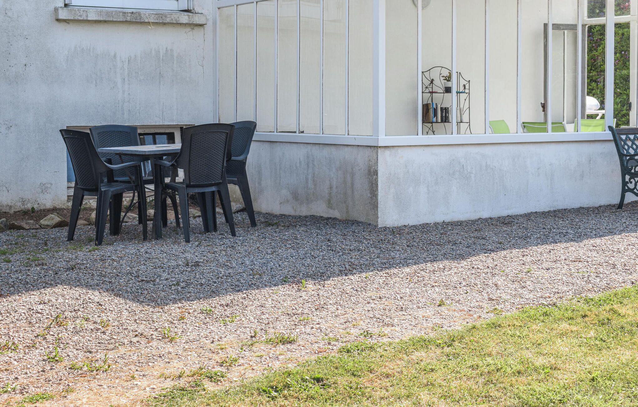 Un patio con mesa y sillas, un jardín pequeño y un invernadero.