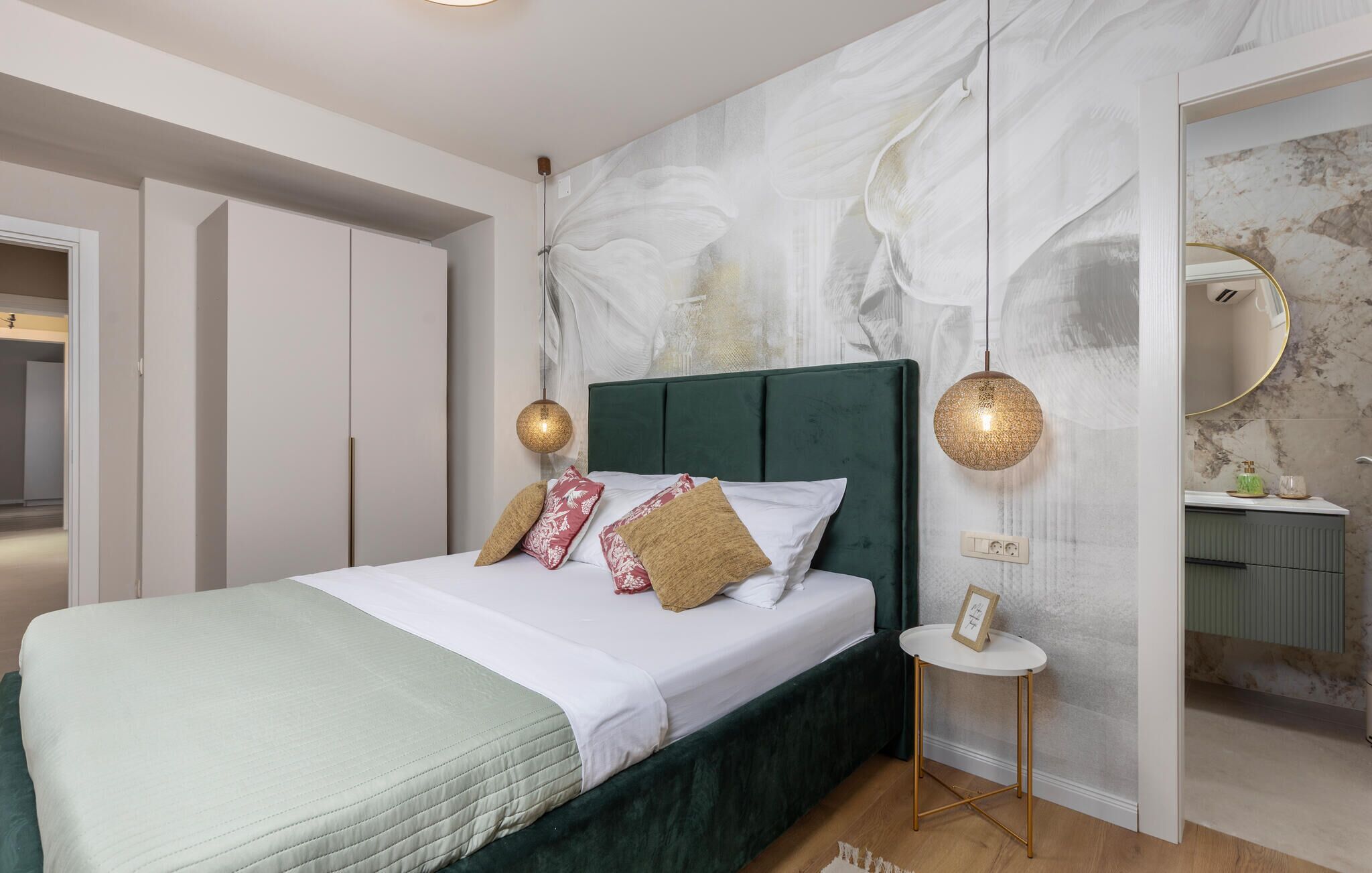 Una camera da letto con una testiera imbottita verde, una coperta bianca e due applique decorative.