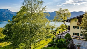 Un refugio de montaña con terraza con vistas a un lago, rodeado de vegetación exuberante y montañas.