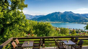 Un patio exterior con mesa y sillas de madera, con vistas a un lago y montañas.