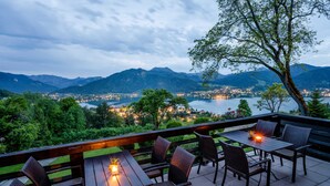 Un área de comedor al aire libre con mesas y sillas, con vista a un lago y montañas.