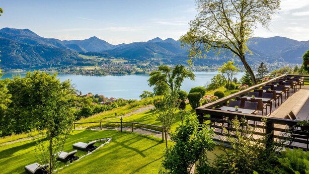 Vista a un lago con zona de comedor, montañas y un césped cuidado.