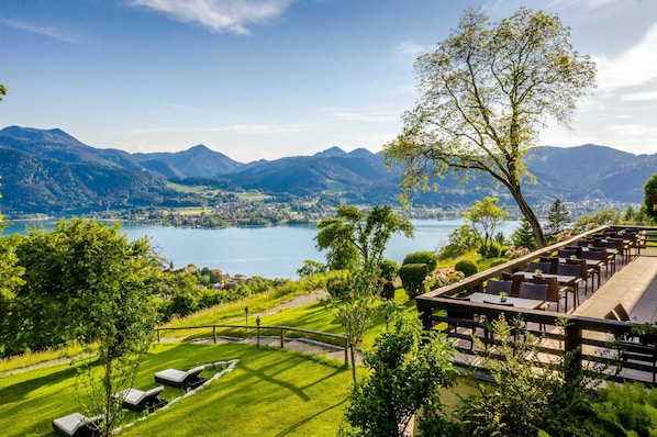 A lakeside view with mountains, a dining area with tables and chairs, and a well-maintained lawn.