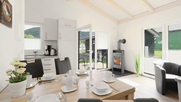 Une cuisine moderne avec des meubles blancs, un coin repas avec une table dressée pour quatre personnes et un poêle à bois.