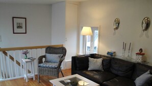 Un salon comprenant un fauteuil en osier, un canapé en cuir noir, une table basse blanche et une table avec un plateau en verre.