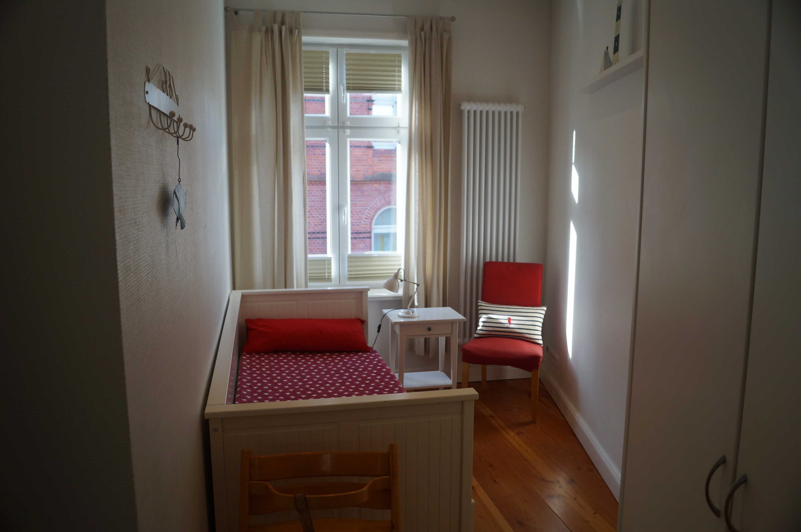 A small bedroom with a bed, a chair, a desk, and a window with curtains.