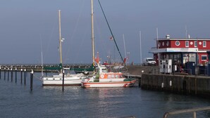 Un quai avec deux bateaux, un bâtiment rouge doté de fenêtres et une jetée qui s’avance dans l’eau.