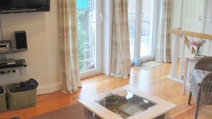 Un salon équipé d’un téléviseur à écran plat, d’une table basse avec un plateau en verre, d’un canapé et d’un fauteuil en osier.