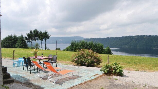 An outdoor seating area with a table and chairs, overlooking a lake and forested hills.