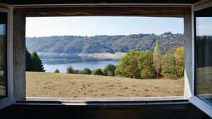 A view through a window of a natural landscape with a lake, trees, and hills.