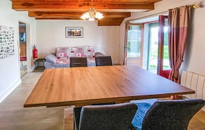 A wooden dining table with four chairs, a patterned sofa, a chandelier, and a view of the outdoors through a glass door.