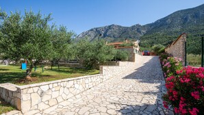 A stone pathway leading to a building with a red-tiled roof, surrounded by greenery and mountains. - Pet friendly home in Desne (Desne)