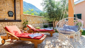 A stone patio with two wooden lounge chairs and a hanging chair. - Pet friendly home in Desne (Desne)