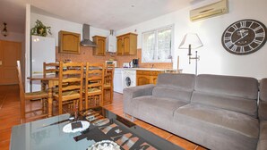 A living room with a grey sofa, wooden dining table with chairs, a glass coffee table, and a kitchen in the background with wooden cabinets and a washing machine. - 3 bedroom awesome home in Casalabriva (Casalabriva)
