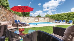 Zona junto a la piscina con sillones de descanso, una sombrilla roja y una mesa con cubierta de vidrio y fresas.