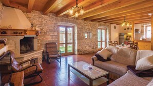 Un interior rústico con chimenea de piedra, sillones de cuero, un sofá y una zona de comedor con techo de madera y paredes de piedra.