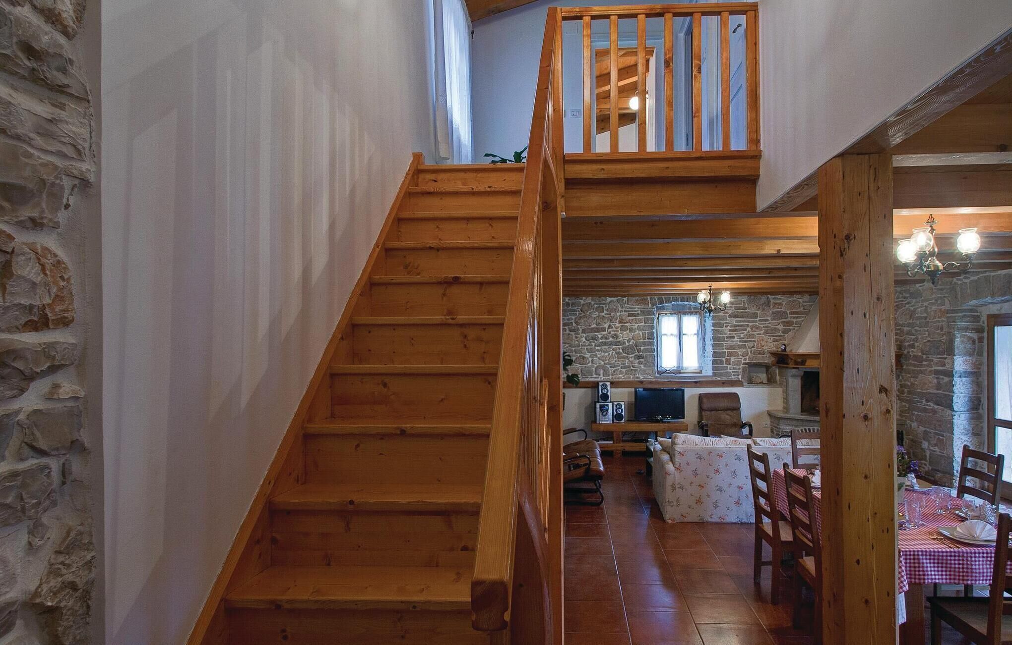 Un escalier en bois mène à un espace de vie aménagé en mezzanine, avec des murs en pierre, une cheminée et une table à manger pour deux personnes.